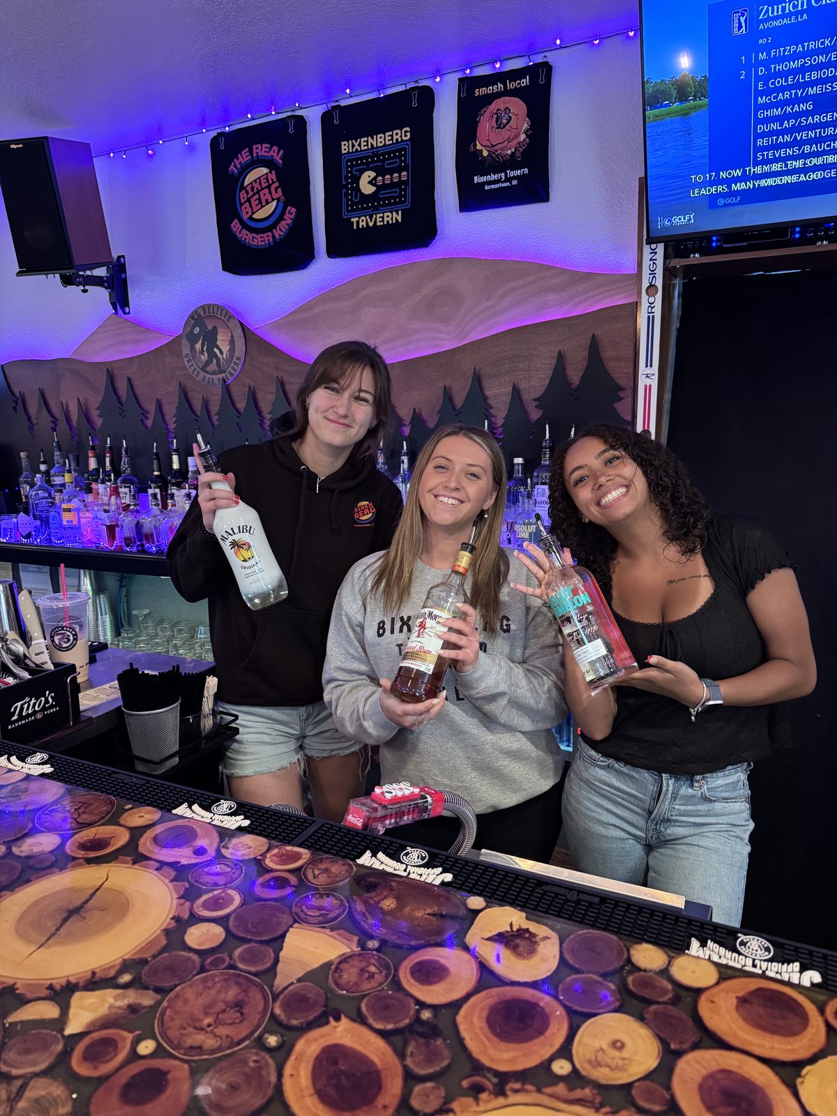 Three bartenders behind the bar with bottles of liquor
